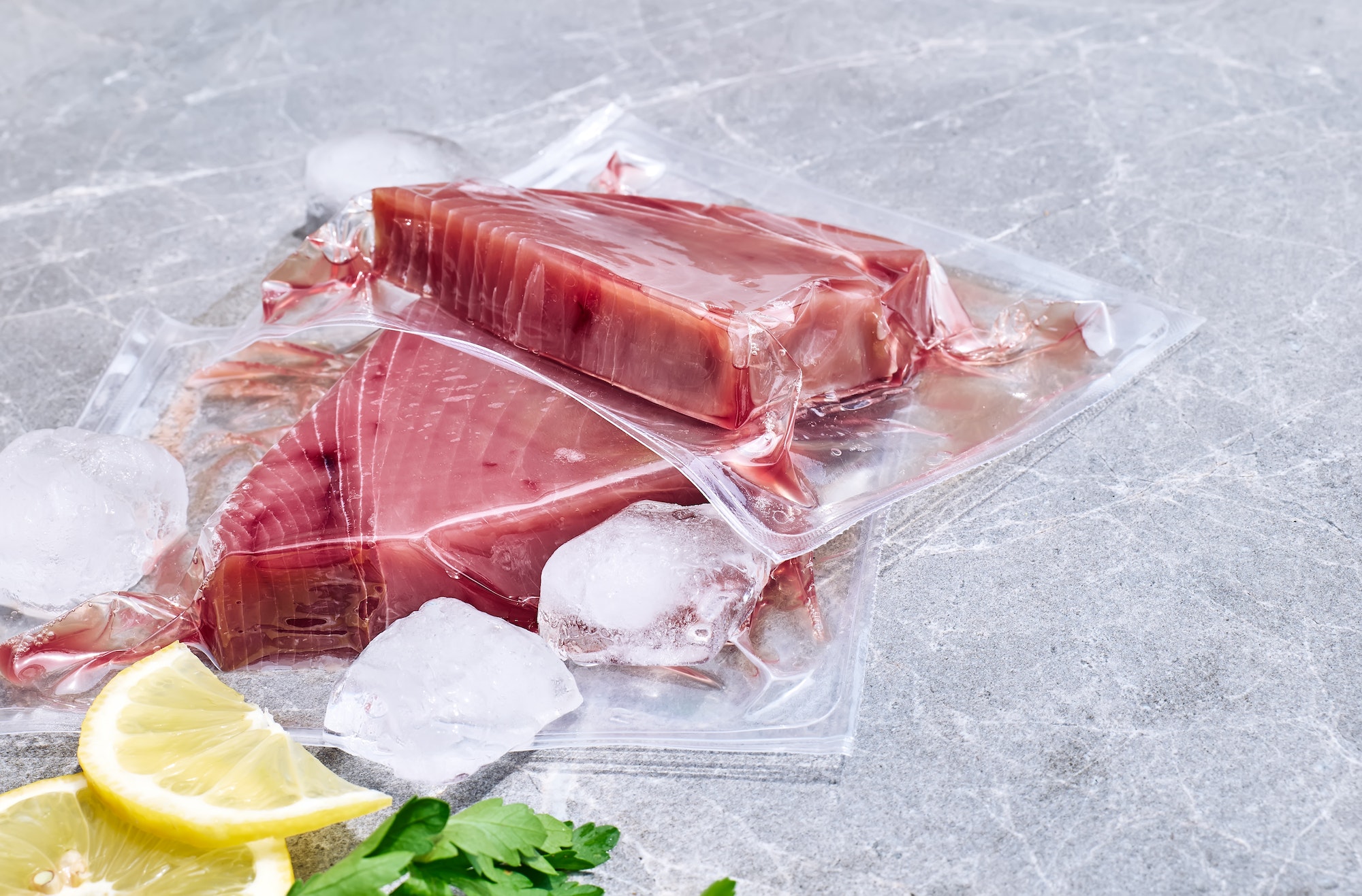 Red tuna fillets in vacuum package on gray marble background.