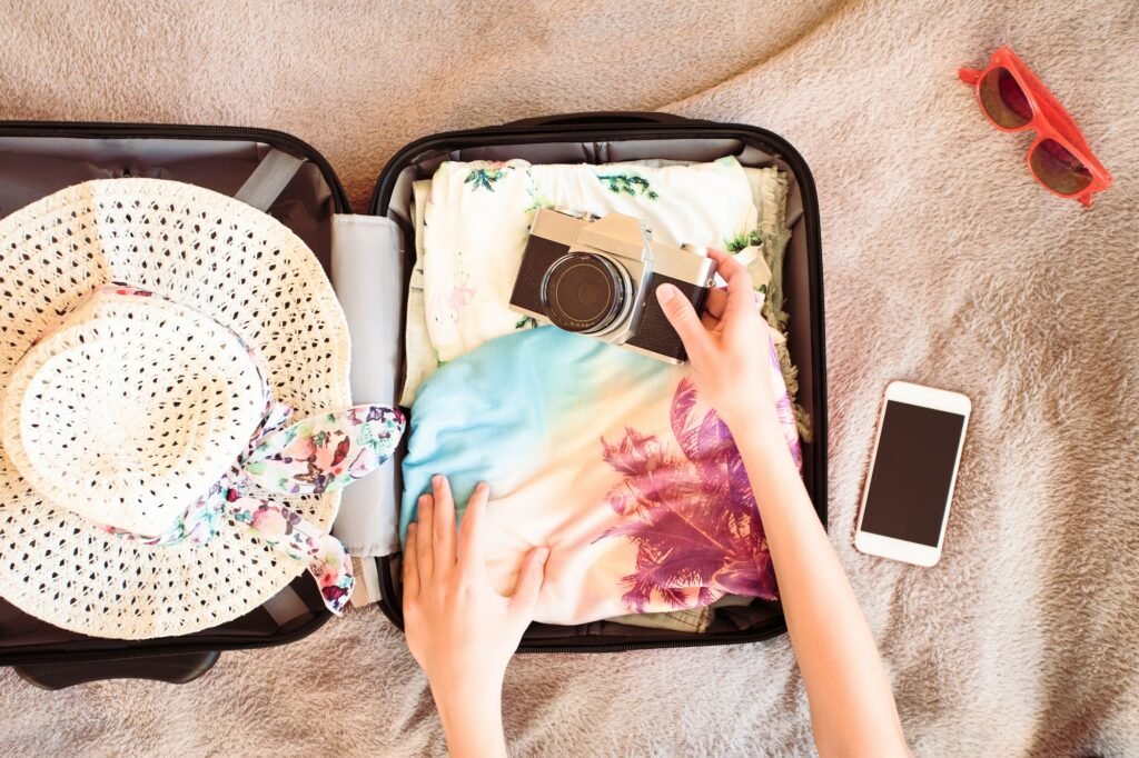 Woman packing suitcase with packed summer clothes, a camera, a hat and sunglasses. Summer vacation